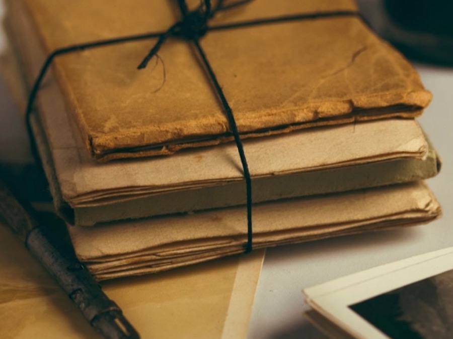 A bundle of old letters tied with twine beside a dip pen and faded photographs